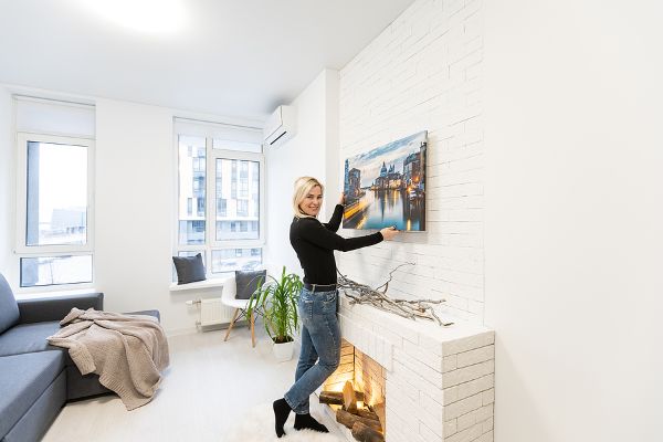 Woman Hanging Canvas Over Fireplace